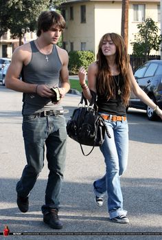 a young man and woman walking down the street with one carrying a handbag in her other hand