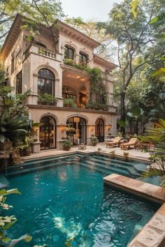 an outdoor swimming pool in front of a large house with lots of trees and plants