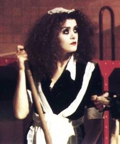 a woman with long hair holding a baseball bat in front of a red bench and wearing an apron