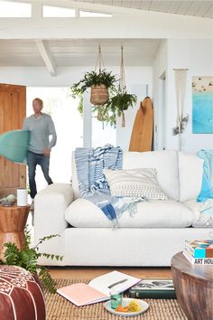 a man standing in front of a white couch with surfboards on the wall behind it