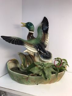 a duck statue sitting on top of a potted plant next to a white wall