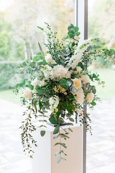 a vase filled with white flowers and greenery on top of a window sill