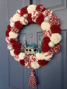 a red and white christmas wreath hanging on a blue front door with ornaments around it