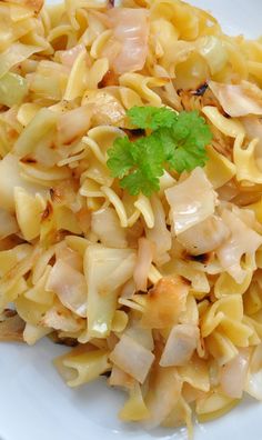 a white plate topped with pasta and meat next to a green leafy garnish