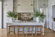 a kitchen island with three stools in front of it and two potted plants on the counter