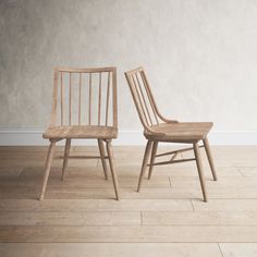 two wooden chairs sitting side by side on a hard wood floor in front of a white wall