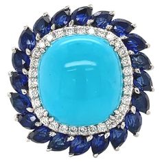 This beautiful cocktail ring features a prong set center blue cabochon turquoise stone weighing 11.60cts. Surrounded by a halo of dazzling round brilliant cut diamonds weighing 1.20cts and pear shaped Blue Sapphires in prong setting weighing 7.39cts. Crafted in highly polished platinum with sparkling round cut diamonds set halfway through the shank. This ring is an absolute one of a kind amazing piece. Diamond quality: G-H color and VVS-VS clarity. Total weight: 23.10 grams. Width: 2.95mm. Ring Blue Diamond Turquoise Ring With Cabochon, White Gold Sapphire, Gold Cocktail Ring, Gold Cocktail, Blue Sapphire Diamond, Diamond Cocktail Rings, Turquoise Rings, White Gold Band, Color Ring