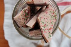 a glass jar filled with pieces of chocolate and sprinkles on top of a table