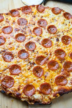 a pepperoni pizza sitting on top of a wooden table next to a spatula