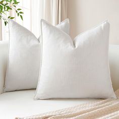 two white pillows sitting on top of a couch next to a plant in a window sill