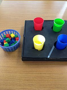 a wooden table topped with plastic cups and legos next to a basket filled with blocks