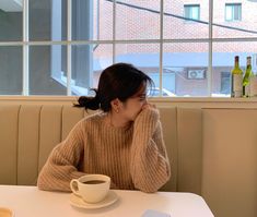 a woman sitting at a table in front of a window with a cup of coffee