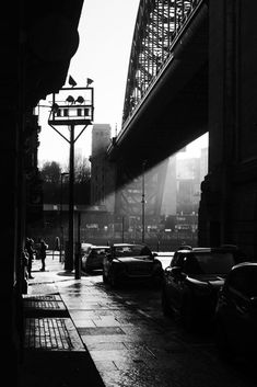 black and white photograph of cars parked on the side of a road under a bridge