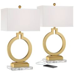 two lamps with white shades on them and a cell phone plugged into the charger