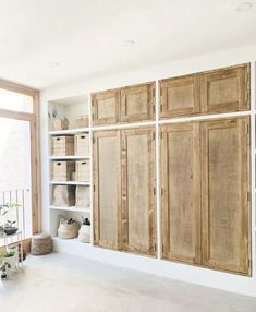 an empty room with wooden cabinets and baskets on the wall, in front of a large window