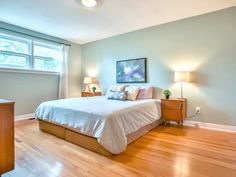 a bedroom with hardwood floors and light blue walls, has a large bed in the corner