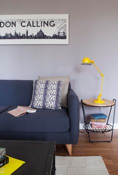 a living room with a blue couch and yellow table in front of the wall that says london calling on it