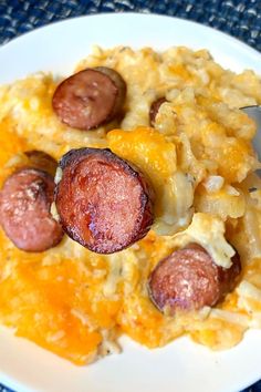 a white plate topped with macaroni and cheese covered in sausages next to a fork