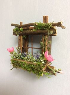 a wooden window with flowers and moss growing in the window sill, on top of a white wall