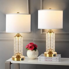 two lamps sitting on top of a white table next to a vase with red flowers