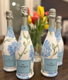 three bottles of wine sitting on top of a wooden table next to a vase filled with flowers