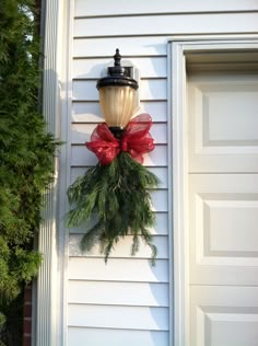 a light hanging on the side of a house with a red bow around it's neck