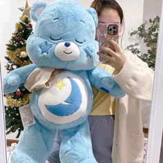 a woman taking a selfie in front of a blue teddy bear holding a phone