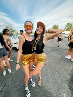 two young women in gold shorts and black tank top posing for the camera with their arms around each other