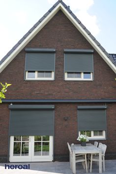 a table and chairs in front of a brick house with shutters on the windows