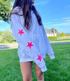 a woman standing in the grass with her back to the camera, wearing a white hoodie with red stars on it