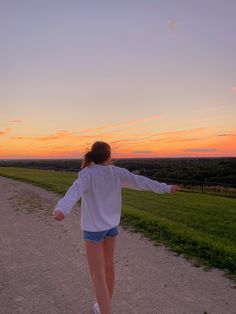 a woman walking down a dirt road at sunset