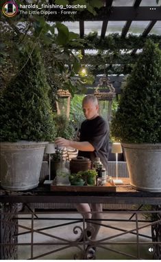 a man standing behind a table filled with potted plants