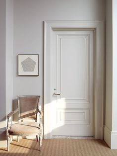 an empty chair in front of a door with a painting on the wall next to it