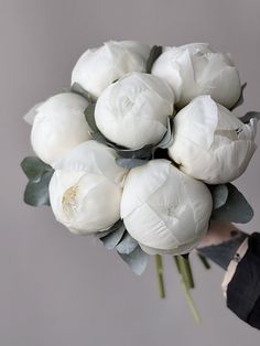 a bouquet of white flowers is held by a woman's hand in front of a gray background