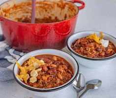 two bowls filled with chili and cheese on top of a table