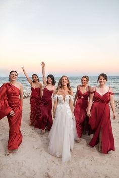 a group of women standing on top of a beach next to each other wearing red dresses