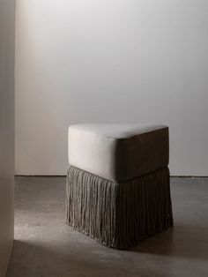 a foot stool with fringe on it in a white walled room next to a wall