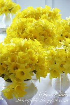 yellow flowers are in white vases on a table