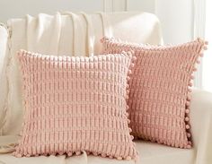 two pink pillows sitting on top of a couch next to a white pillow case with pom - poms