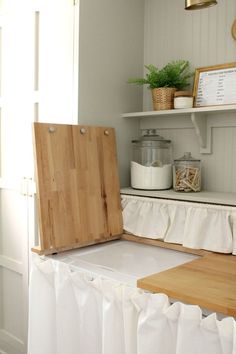 a wooden cutting board sitting on top of a counter next to a white cabinet and window