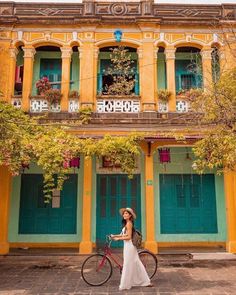 a woman standing next to a bike in front of a building with green and yellow doors