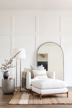 a living room with white walls and wood flooring, a large mirror on the wall