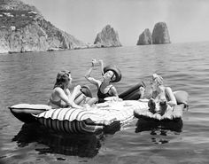 three women sitting on rafts in the water with rocks in the background and one woman holding a bottle