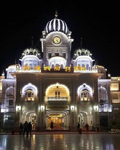 people are standing in front of a large building with lights on it's sides