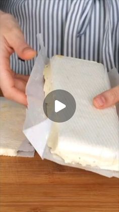 a person cutting cheese on top of a wooden table with a piece of paper in front of them