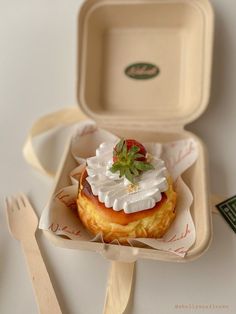 a small pastry with whipped cream and strawberries on top in a paper tray next to utensils