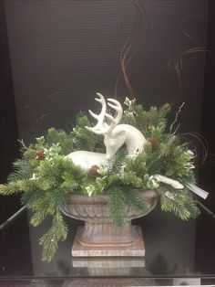 a vase filled with greenery and white deer figurines on top of a table