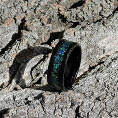 a black ring with blue and green opal inlays on top of a rock