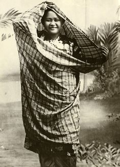 an old black and white photo of a woman carrying a blanket over her head with palm trees in the background