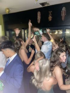 a group of people dancing at a party with their arms in the air and one person wearing a suit